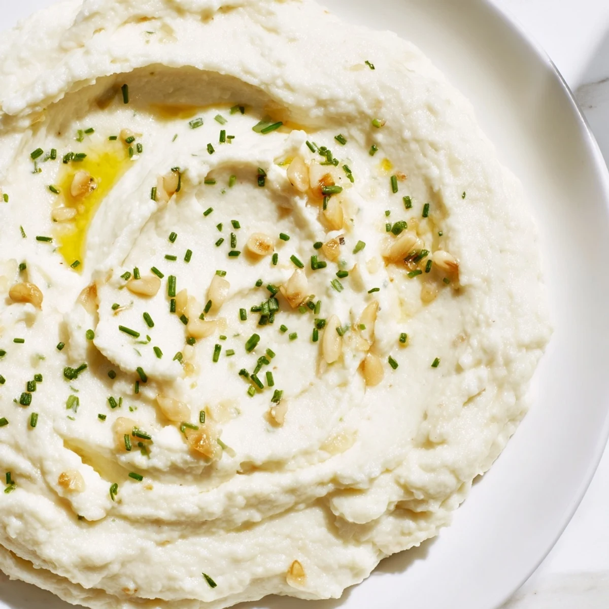 A bowl of creamy Roasted Garlic Mashed Cauliflower, garnished with fresh chives, ready to eat.
