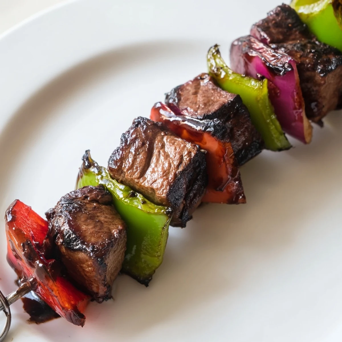 Grilled Beef Kebabs with Bell Peppers and Red Onion sizzling on a platter with charred edges and fresh herbs.