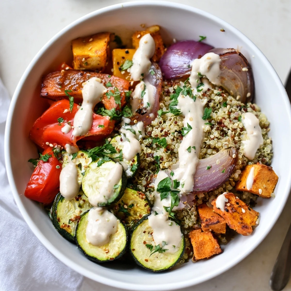 A close-up of Roasted Vegetable Quinoa Bowl with Tahini featuring fluffy quinoa, caramelized red onion, and cherry tomatoes, finished with toasted sesame seeds.