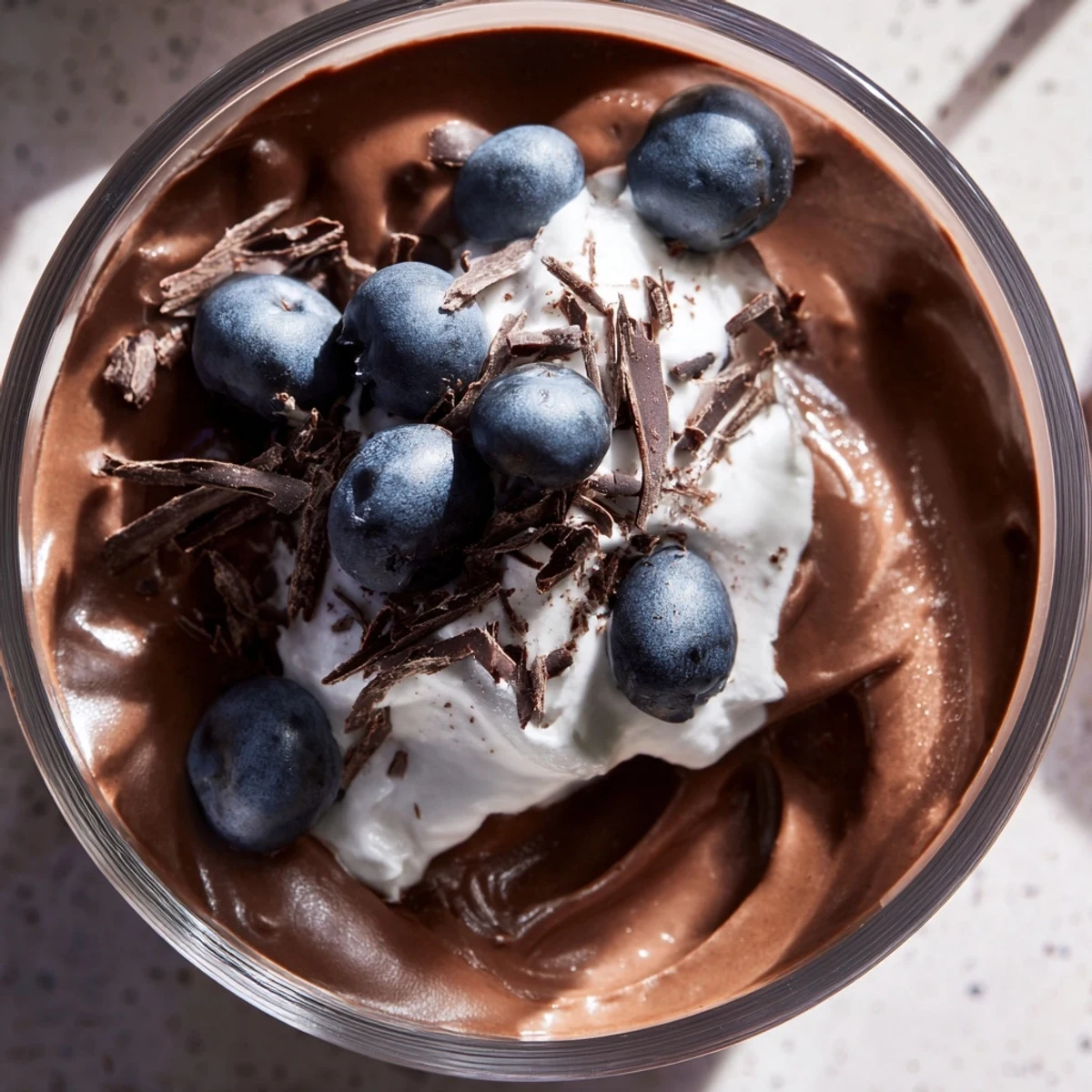 A close-up of Chocolate Avocado Mousse topped with a swirl of coconut cream and dark chocolate shavings.