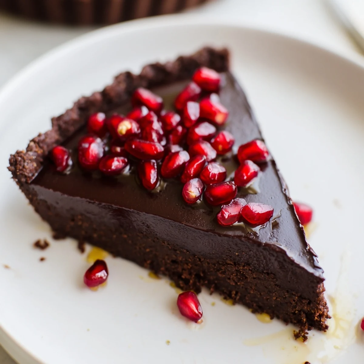 A close slice of the Valentine Chocolate Pomegranate Tart shows ruby-red pomegranate arils sparkling on rich, smooth ganache.