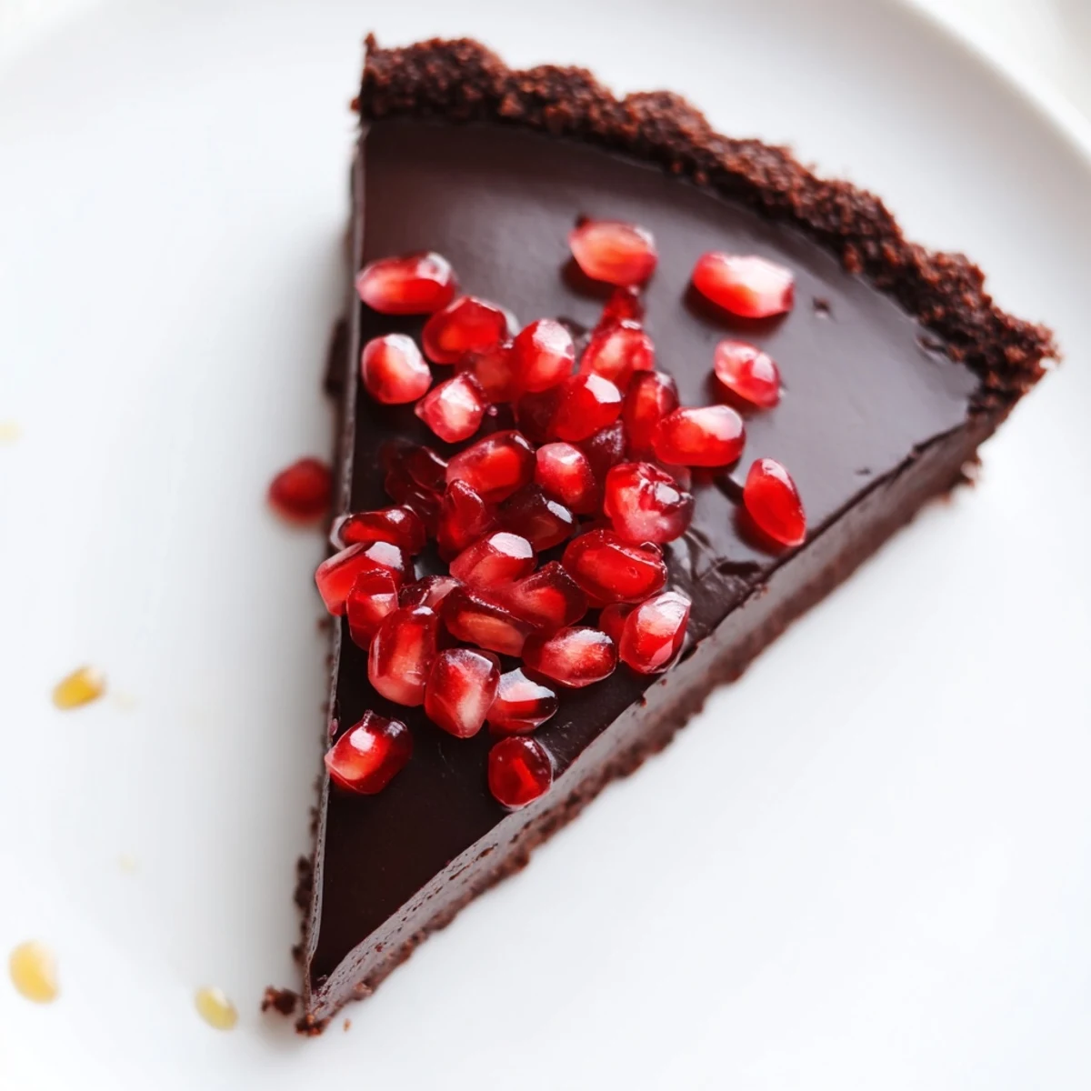 The whole Valentine Chocolate Pomegranate Tart sits on a marble counter, garnished with a light drizzle of honey and sea salt.