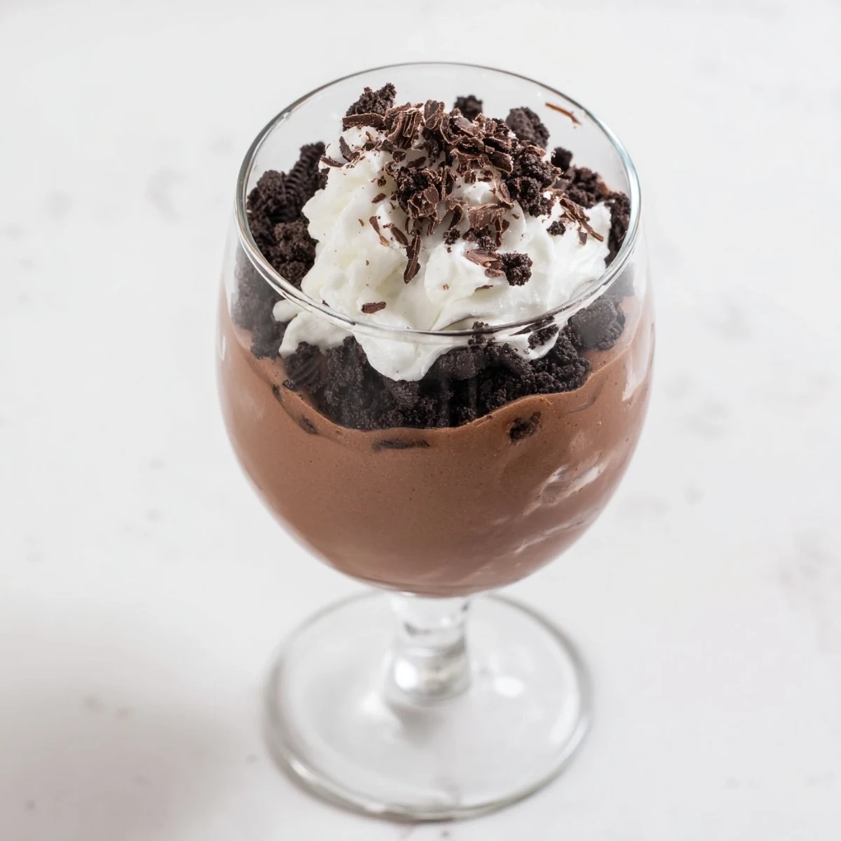 Silky chocolate pudding layered with crunchy cookie crumbs and fluffy whipped cream in a clear glass.
