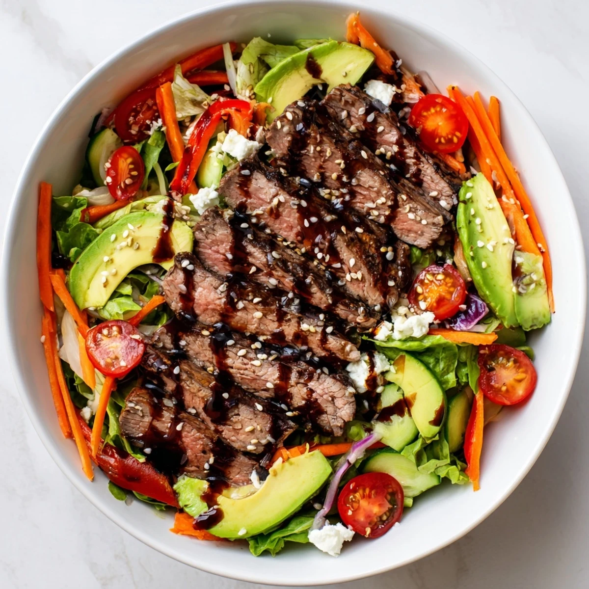 This healthy beef salad bowl features sliced steak over mixed greens with avocado, cucumber, and tomatoes.