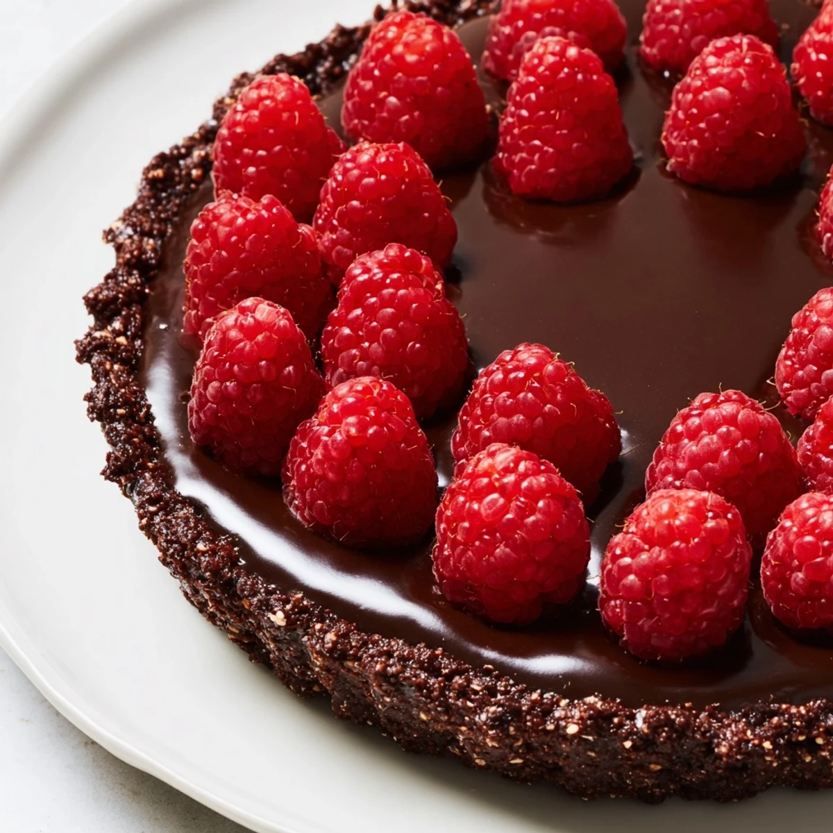 Sliced wedge of Chocolate Raspberry Tart with Ganache shows layers of chocolate crust, rich ganache, and fresh raspberry garnish.  