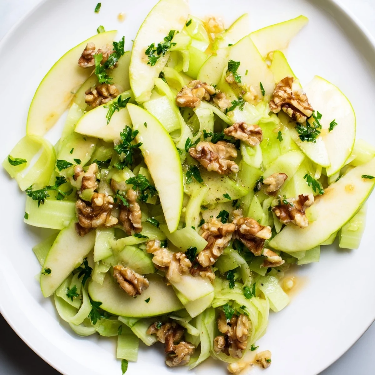 Freshly sliced green apples and celery tossed with toasted walnuts and a light tangy dressing in a bowl.