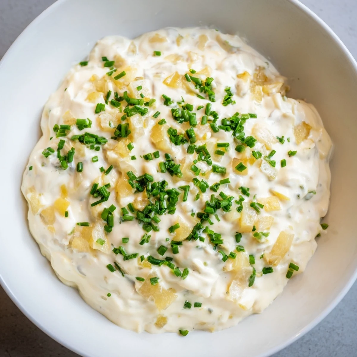 Creamy Game Day Onion Dip with Potato Chips sits in a rustic bowl, garnished with fresh chives.