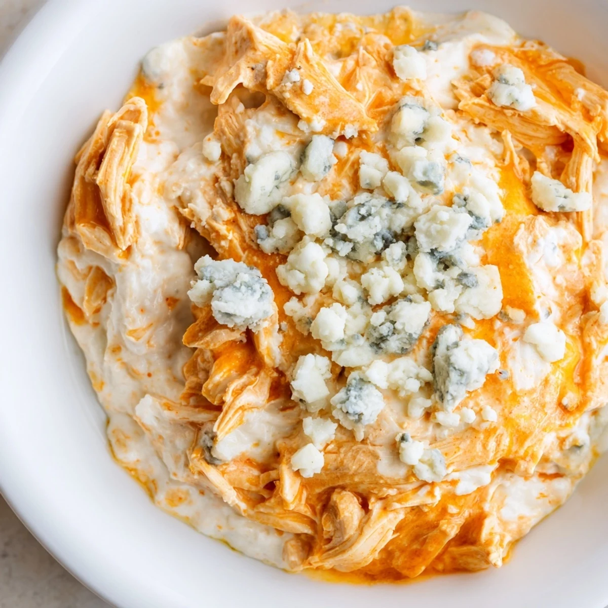 A warm, bubbly Spicy Buffalo Chicken Dip in a skillet, topped with melted mozzarella and crumbled blue cheese, served with crisp celery sticks for dipping.  