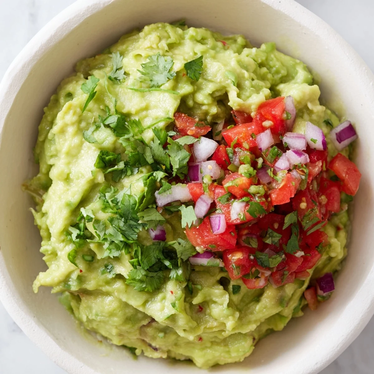 Homemade guacamole topped with zesty pico de gallo and a squeeze of fresh lime, served in a rustic bowl.  