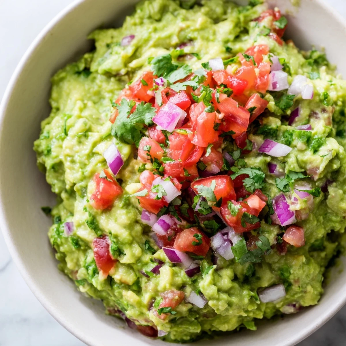 A vibrant bowl of creamy guacamole with fresh pico de gallo and lime, perfect for dipping with tortilla chips.  