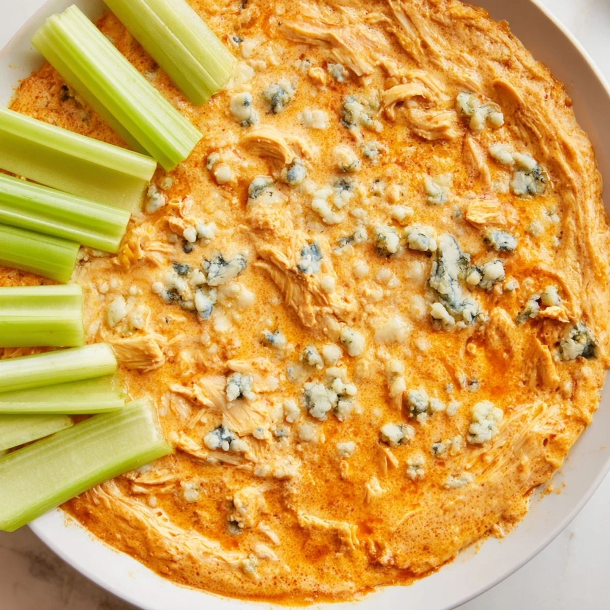 Fresh celery sticks piled beside a warm bowl of Spicy Buffalo Chicken Dip, perfect for a game day appetizer spread.