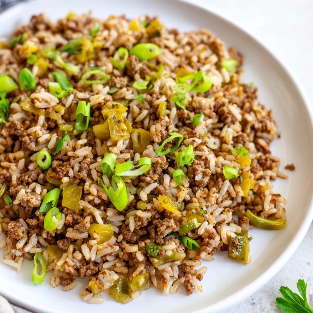 A close-up photo of Cajun dirty rice with ground beef, featuring browned meat, aromatic vegetables, and fluffy white rice garnished with fresh parsley and green onions.