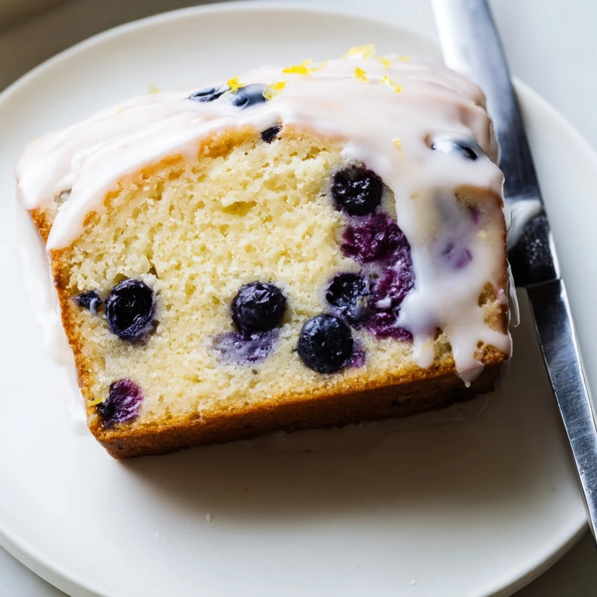 A rustic loaf pan of Lemon Blueberry Yogurt Loaf Cake, drizzled with lemon glaze and perfect for breakfast or dessert.