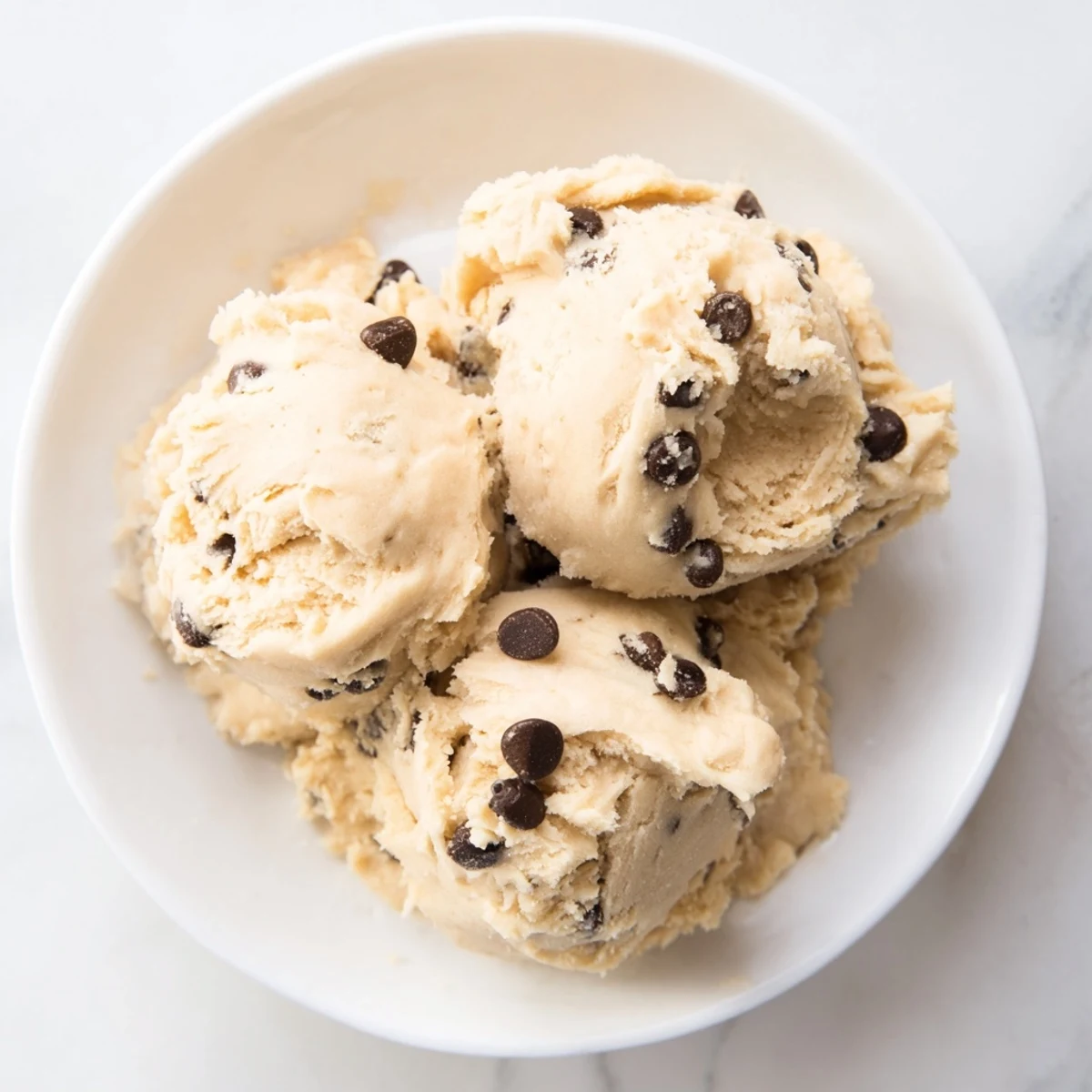 Golden-brown Edible Keto Cookie Dough scoops sit atop a rustic wooden board, with sugar-free chocolate chips glistening in the light.