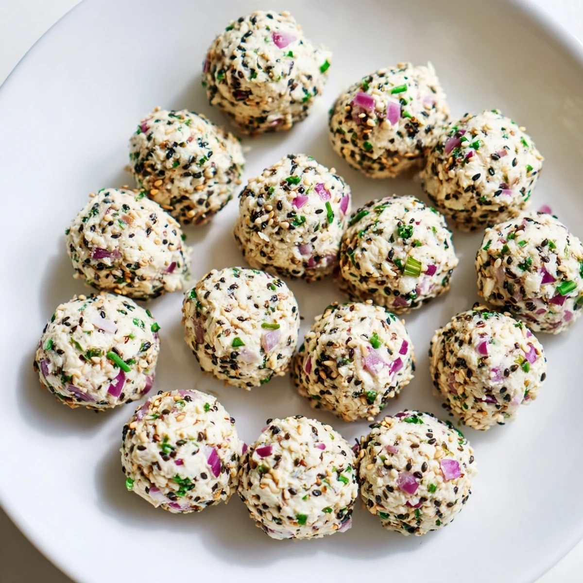 Freshly rolled Everything Bagel Cottage Cheese Bites coated in savory seasoning and chives on a white plate.