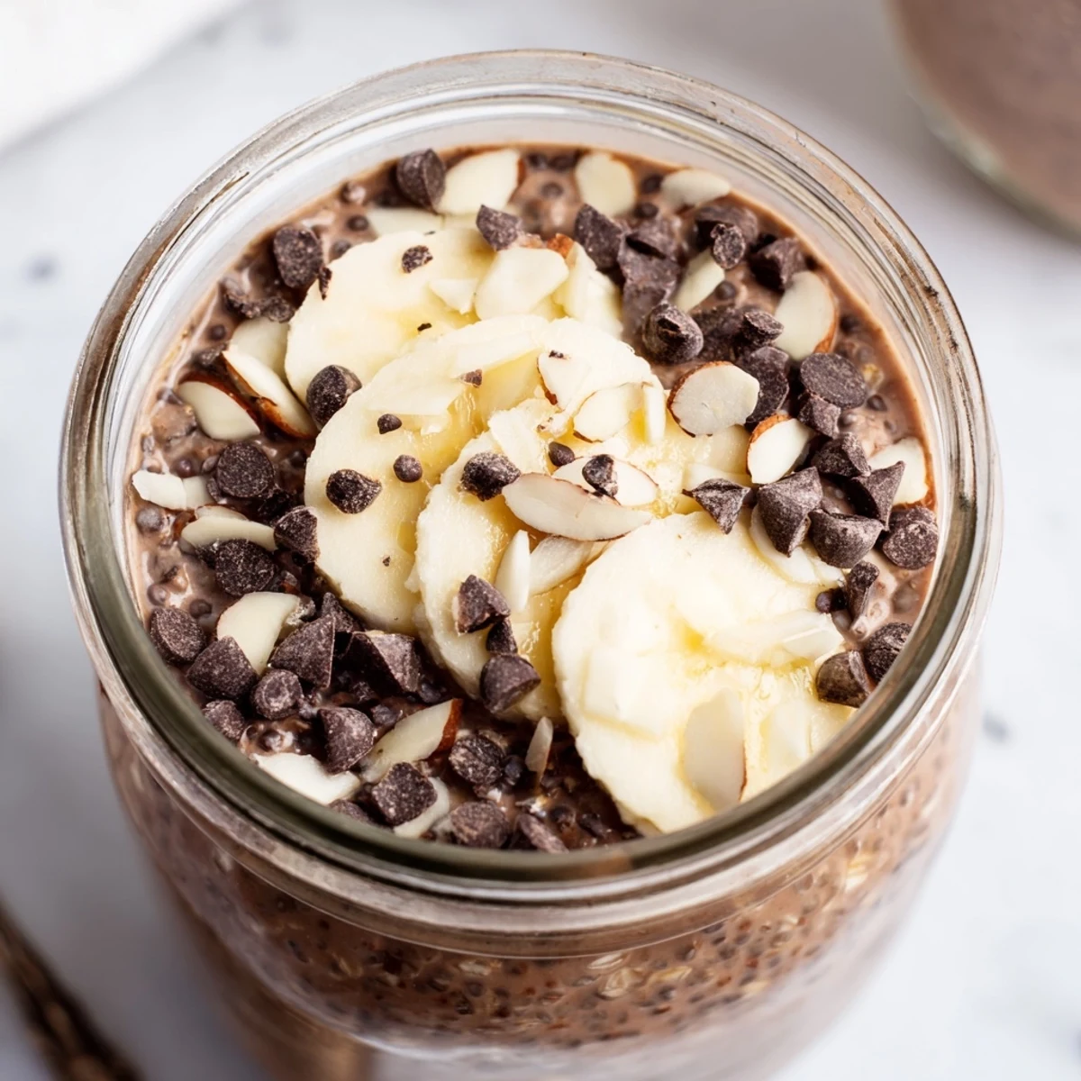Creamy Ultimate Healthy Chocolate Overnight Oats topped with banana slices and chopped nuts, served in a clear jar.