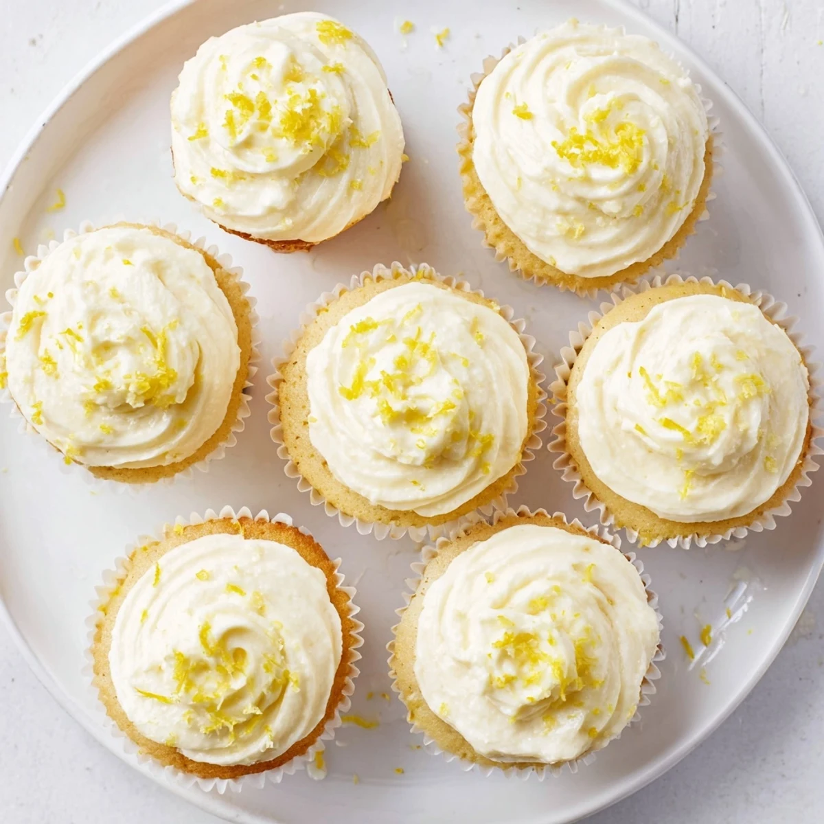 Frosted Limoncello Cupcakes with tangy lemon buttercream swirls and bright zest on a rustic wooden board.