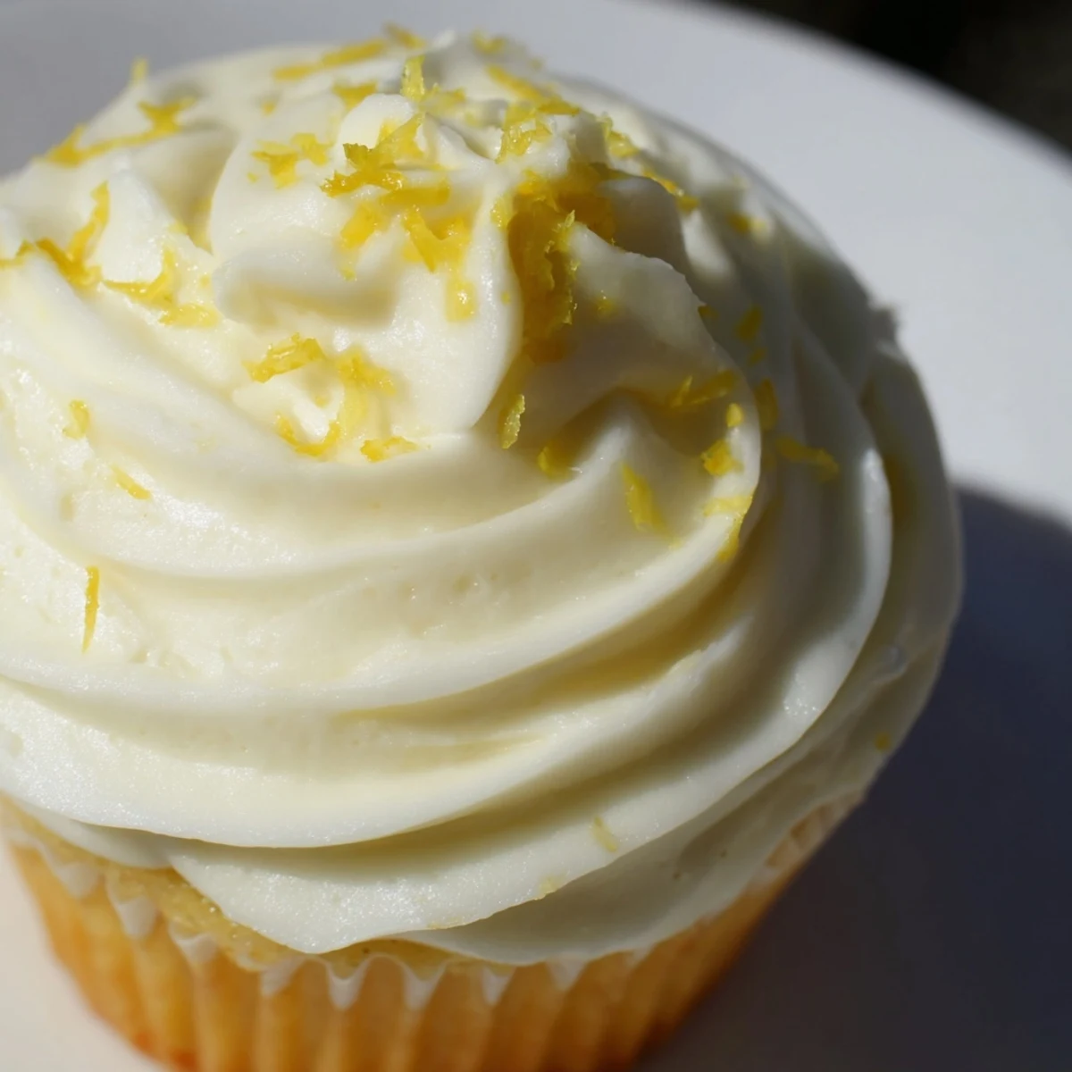 Freshly baked Limoncello cupcakes topped with creamy lemon frosting, showcased on a rustic wooden table with vibrant lemon slices.  