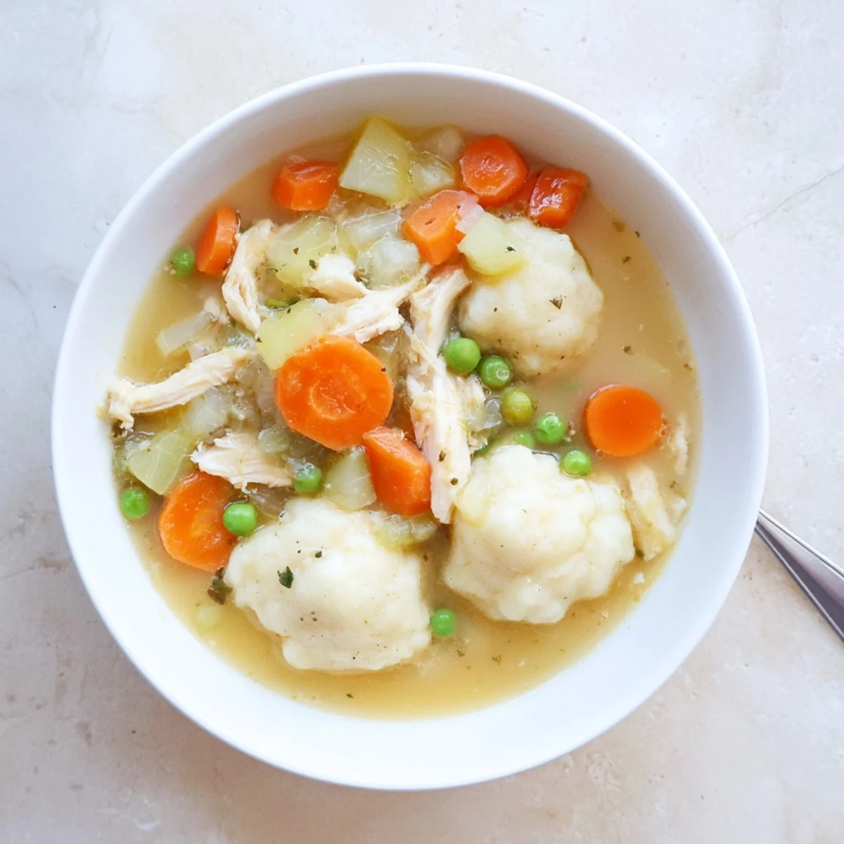 A close-up of One Pot Chicken Dumpling Soup showing plump dumplings, shredded chicken, and vibrant peas in a rich, steaming broth.