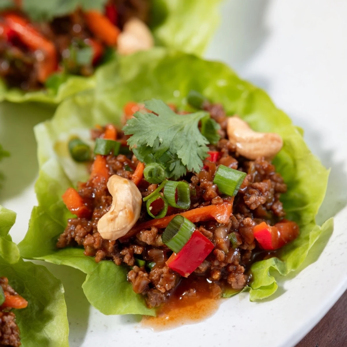 Asian-inspired beef and cashew lettuce cups featuring colorful diced vegetables and fresh coriander on a white serving plate