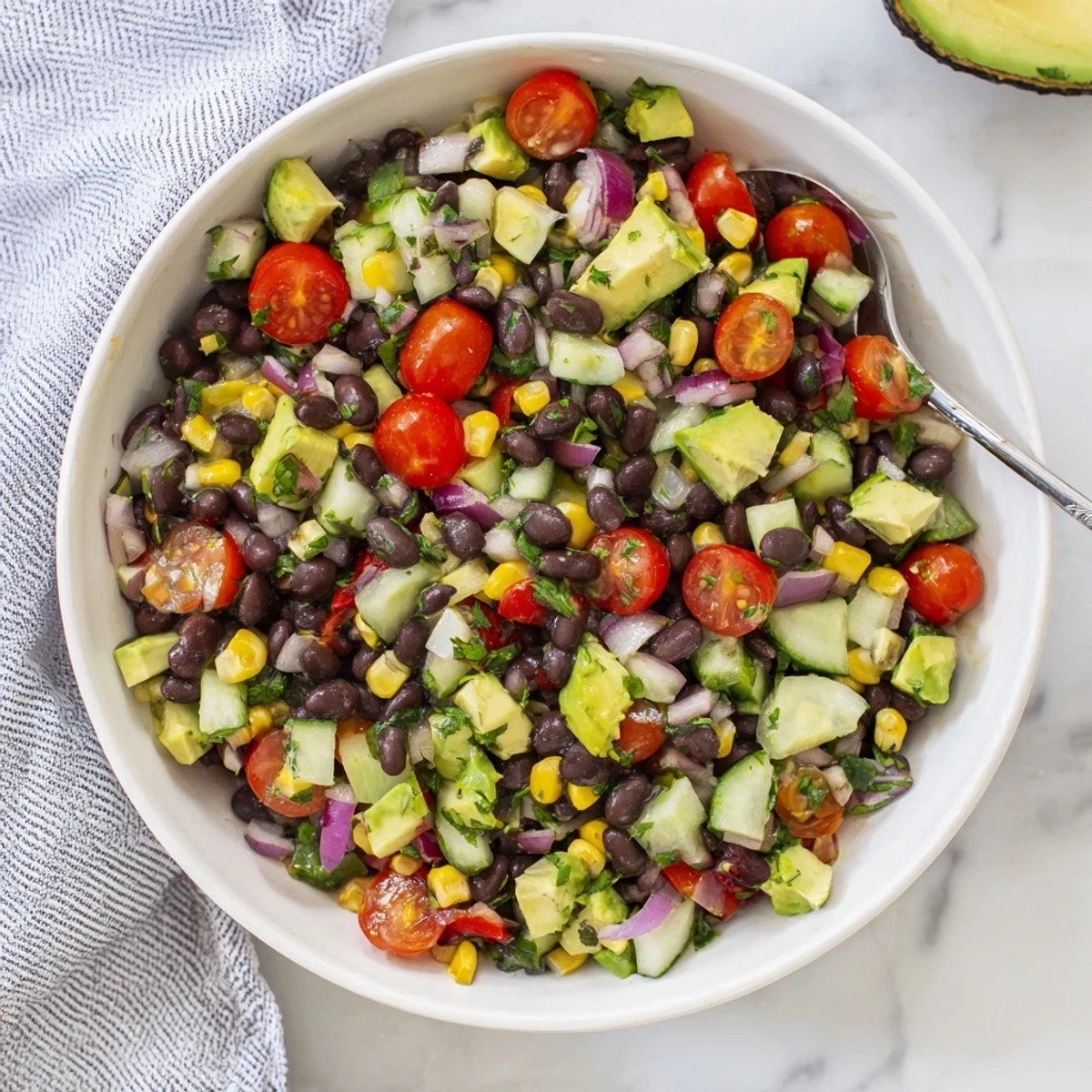 Colorful chopped black bean salad bowl with fresh corn, diced avocado, and crisp vegetables drizzled with lime dressing