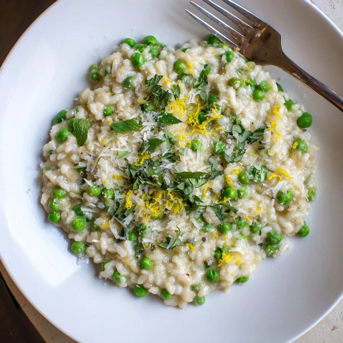 Creamy spring pea risotto topped with grated Parmesan and fresh green herbs in a shallow white bowl