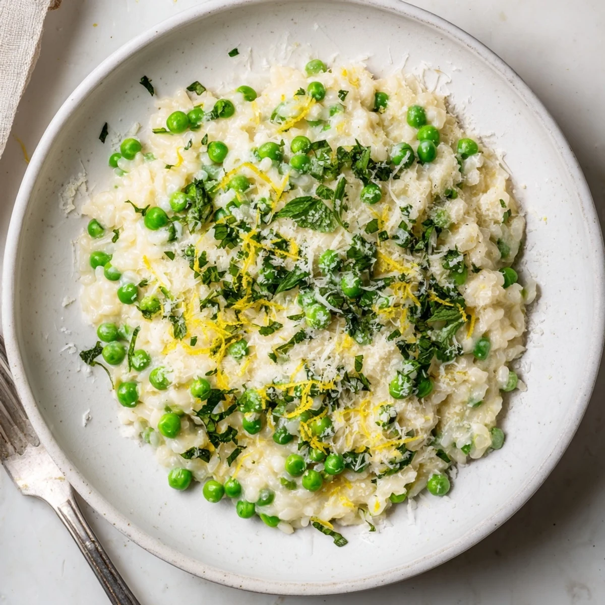 Spoonful of spring pea risotto garnished with chopped parsley and extra Parmesan cheese shavings