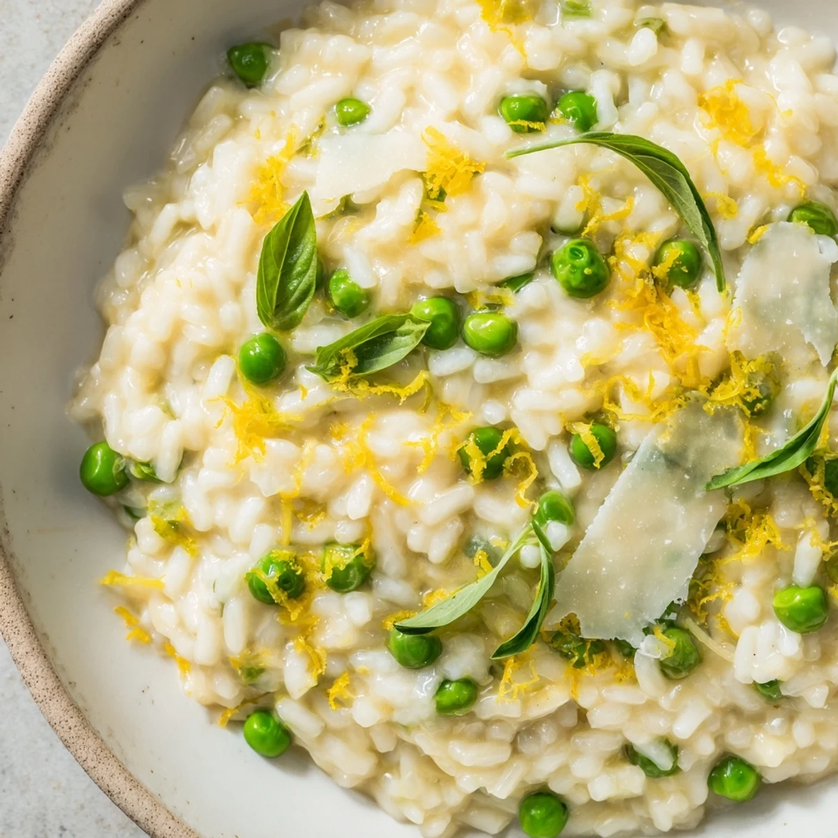 Creamy spring pea risotto with bright green peas, fresh basil, and grated Parmesan cheese in a shallow bowl