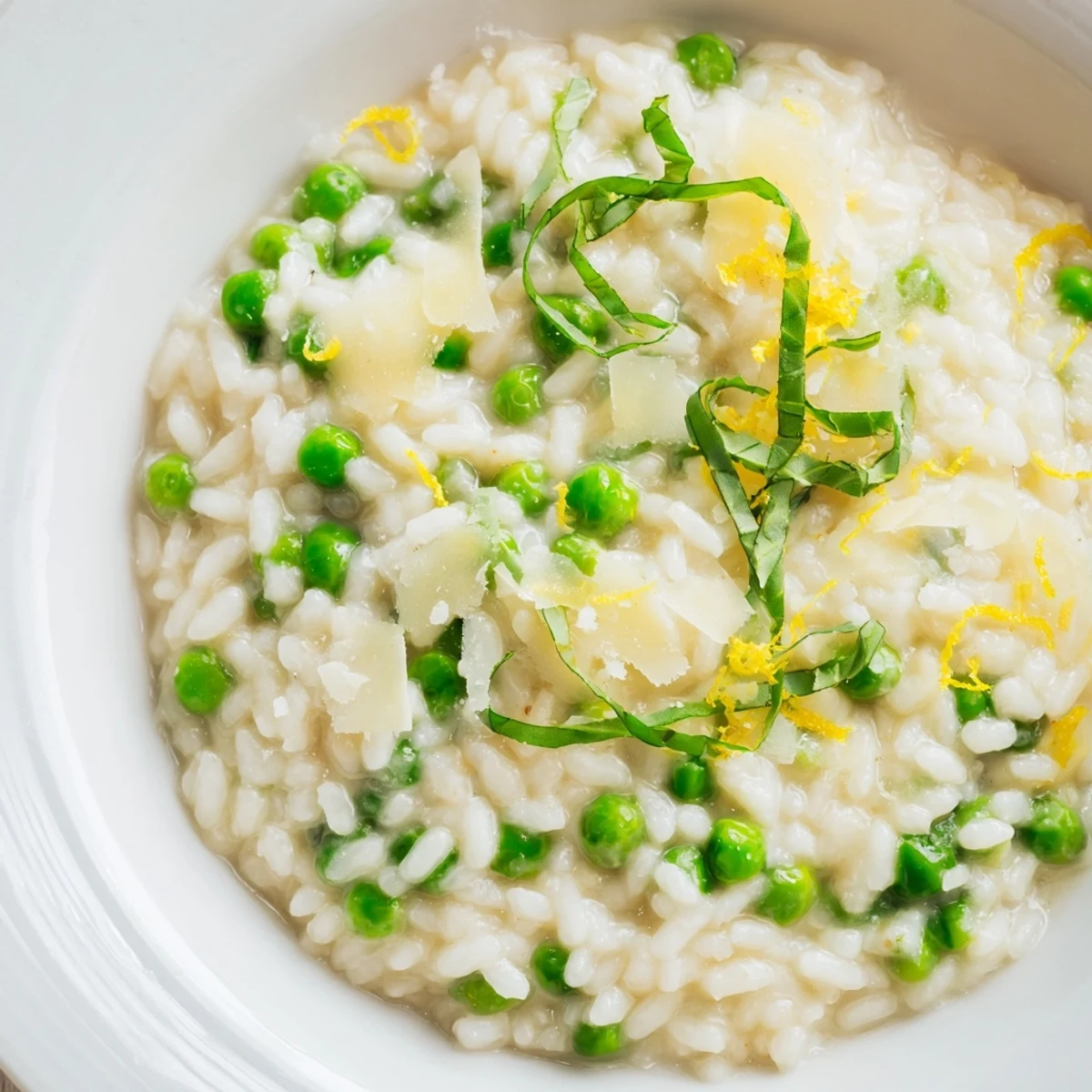 Close up of Spring pea risotto topped with fresh basil chiffonade and extra Parmesan on a white plate