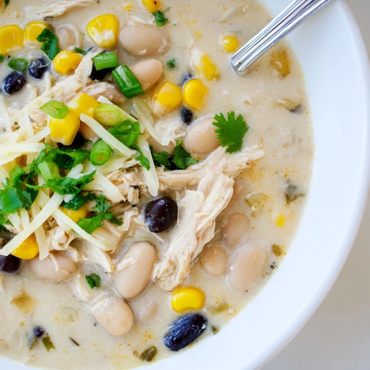 Spoonful of rich white chicken chili featuring tender shredded chicken and corn kernels