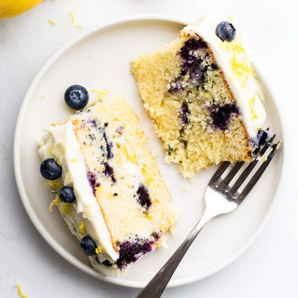 Two-layer lemon blueberry cake topped with creamy frosting and scattered fresh blueberries