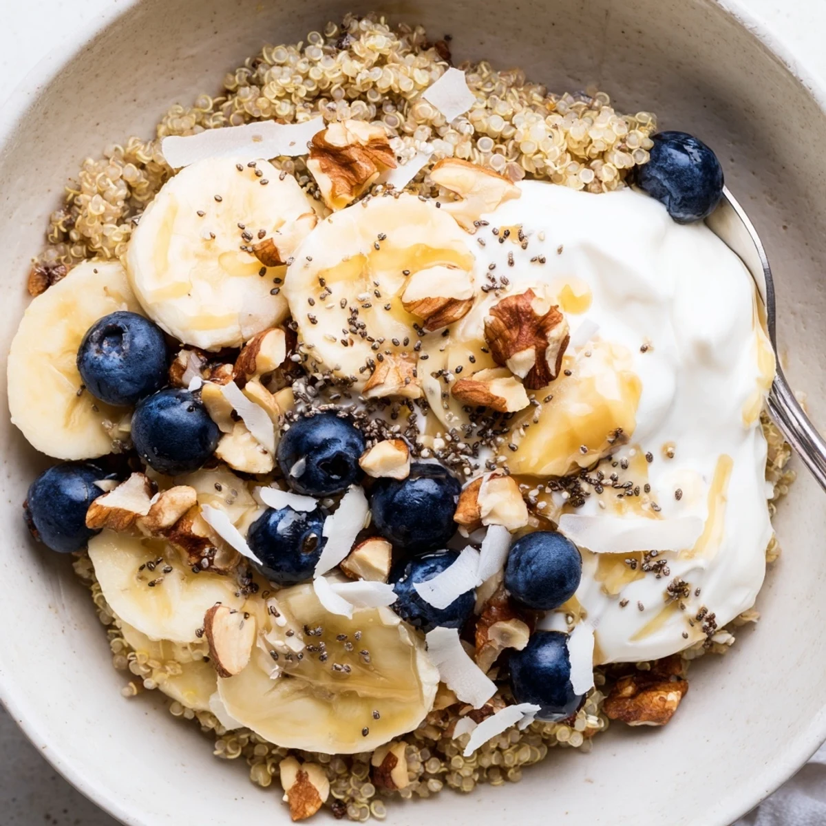 Creamy blueberry quinoa breakfast bowl topped with fresh fruit, crunchy nuts, and coconut flakes