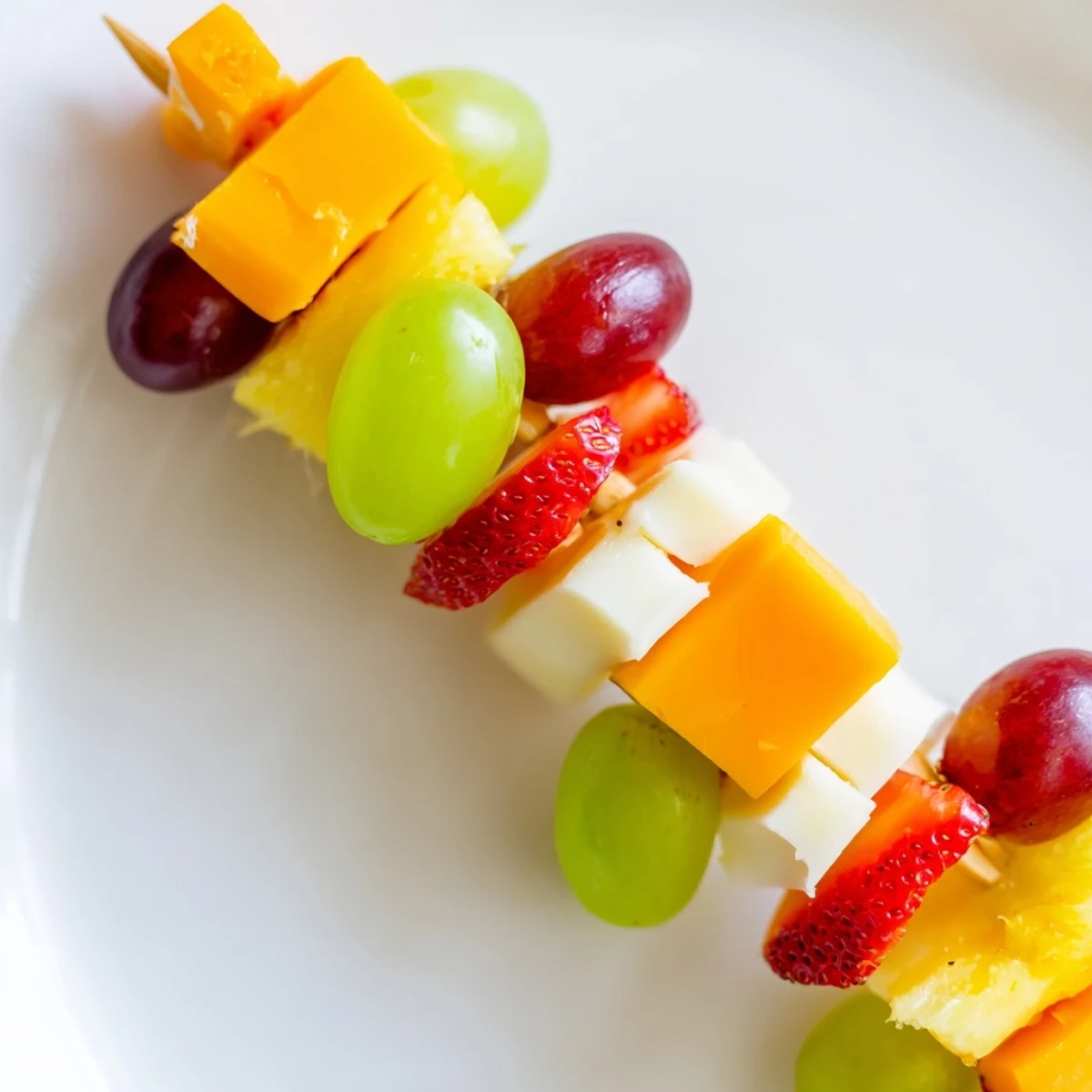 Colorful fruit and cheese kabobs arranged on a white platter with fresh mint garnish