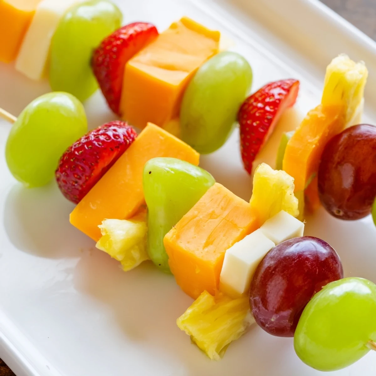 Fruit and cheese kabobs featuring red grapes pineapple strawberries and cubed cheddar cheese