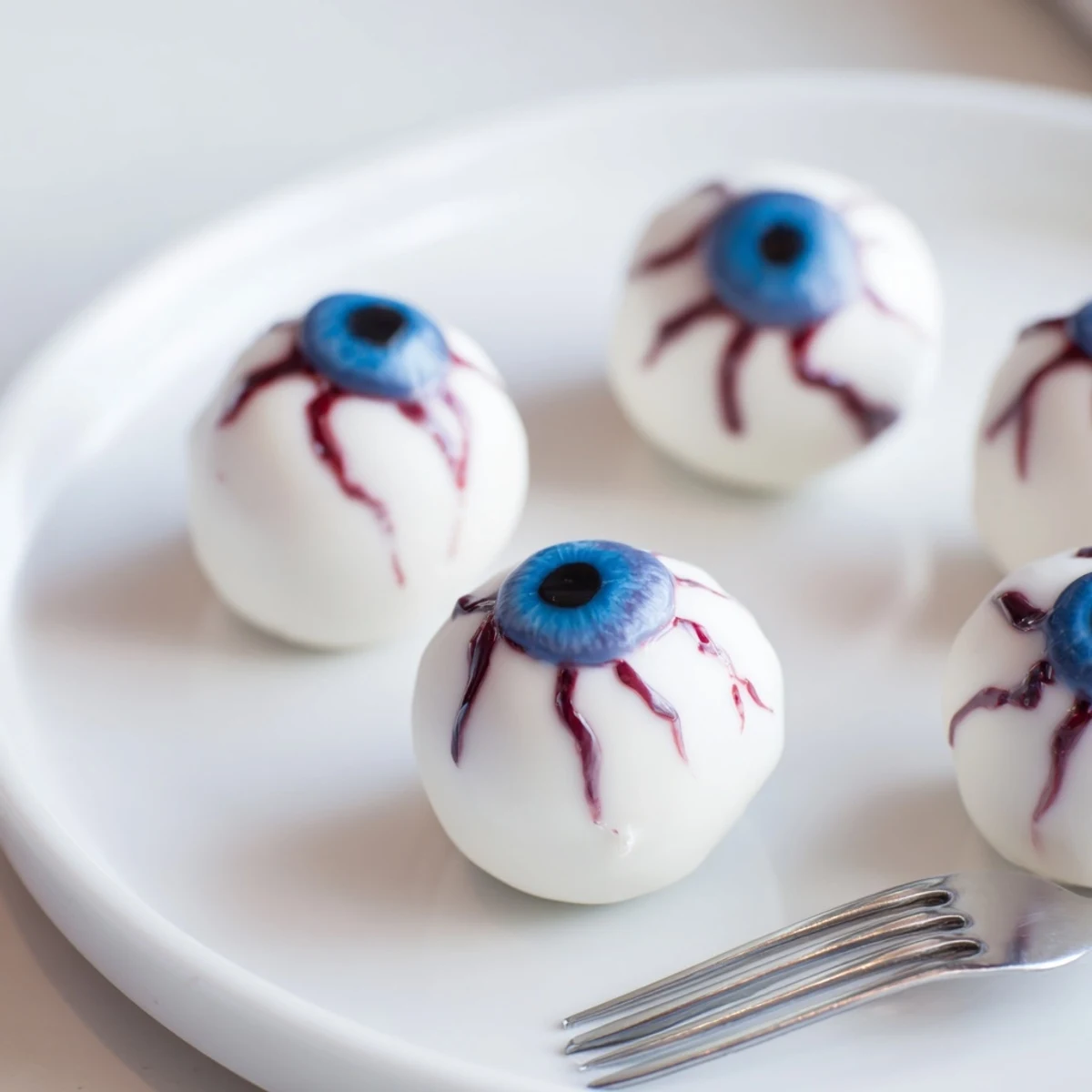 Halloween Cake Eyeballs with red veins, blue irises, and smooth white chocolate coating on a dark platter