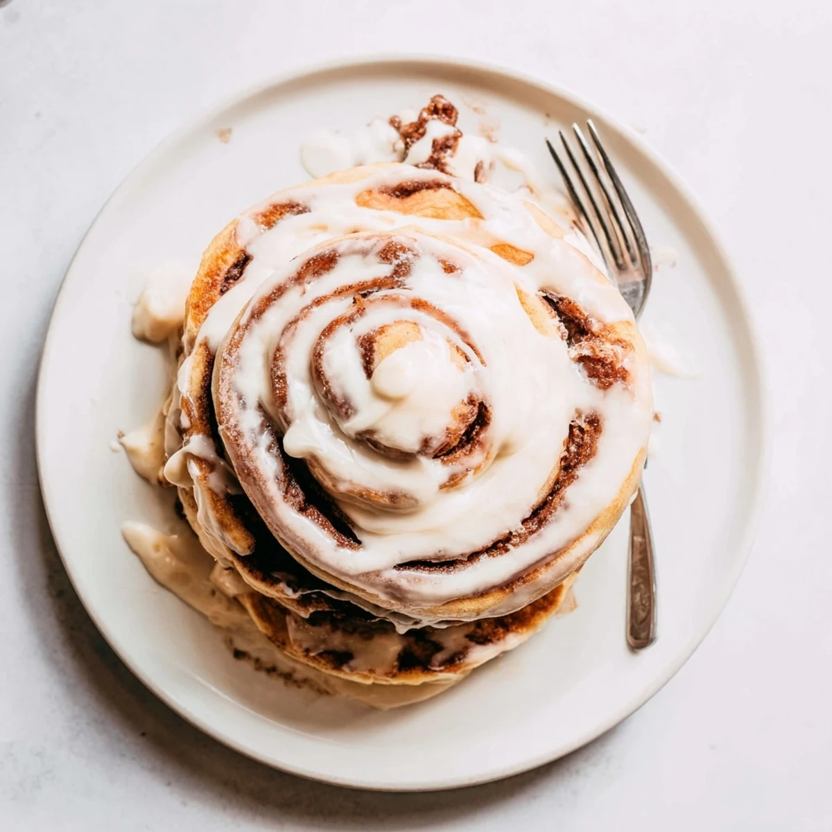Golden cinnamon roll pancakes stacked high with rich cream cheese icing drizzle