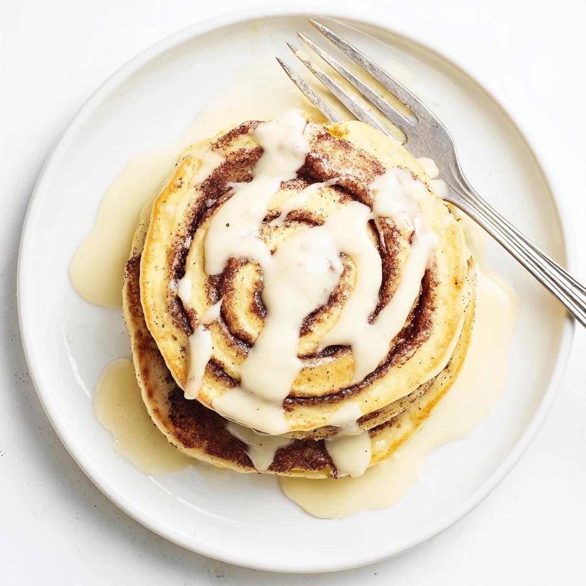 A stack of cinnamon roll pancakes dripping with sweet cream cheese glaze