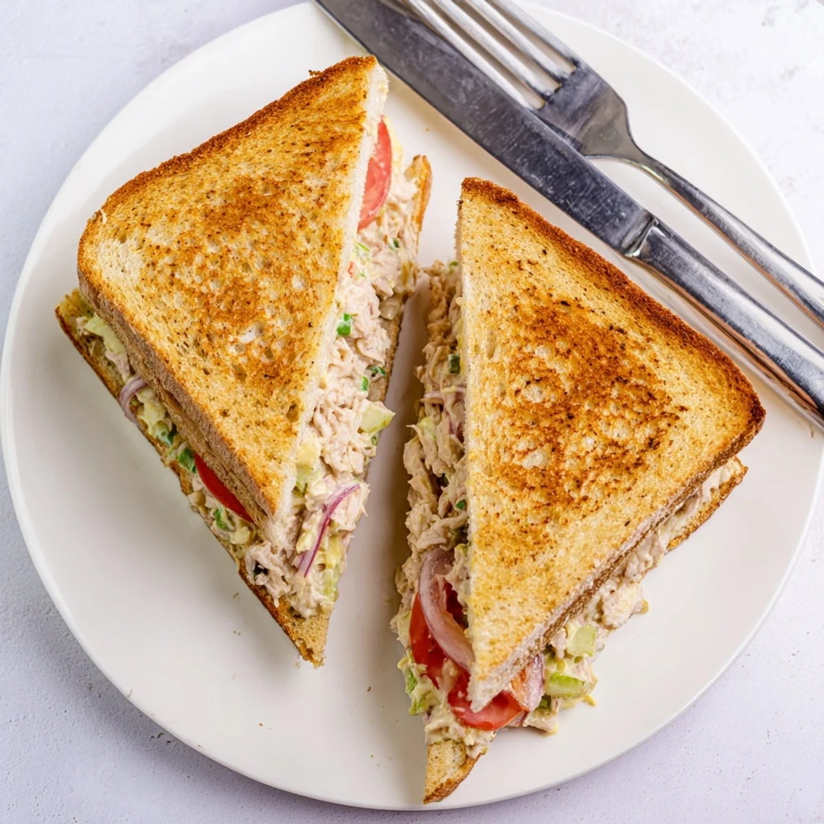 Hot skillet-cooked tuna melt sandwich cut in half revealing layers of melted cheese and seasoned tuna