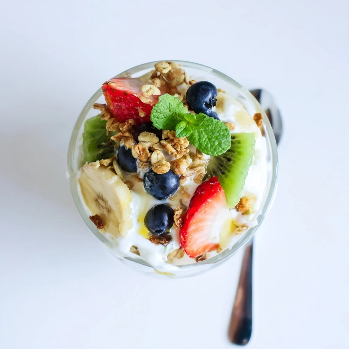 Glass parfait bowl showing creamy Greek yogurt layered with colorful mixed fruits and honey