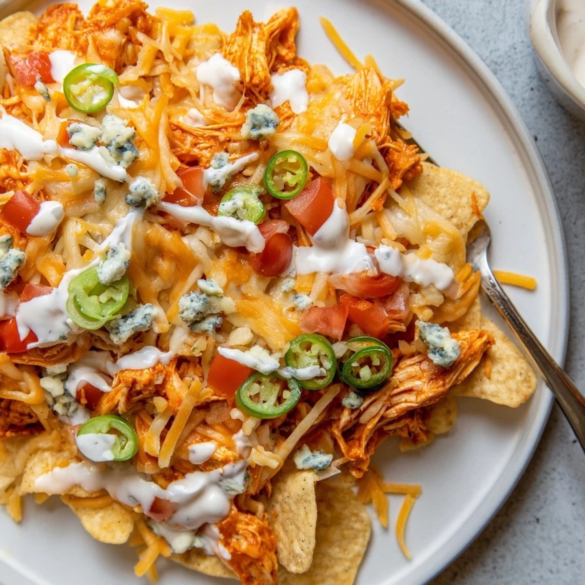Game-day Buffalo Chicken Nachos topped with blue cheese crumbles and fresh tomatoes