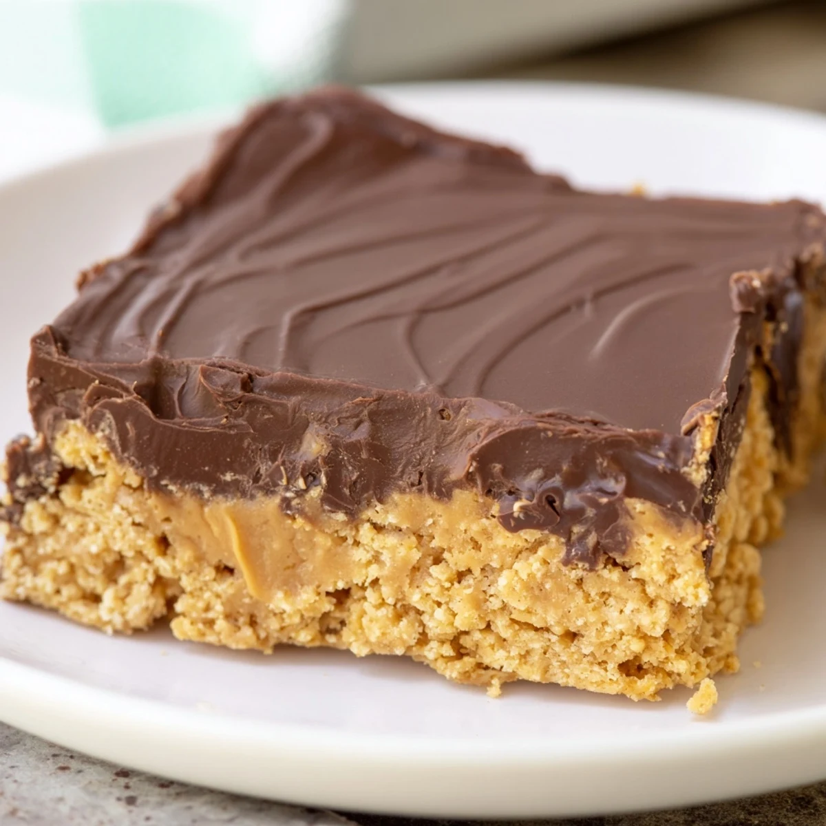 Rich peanut butter bars with glossy chocolate topping displayed on a white serving plate