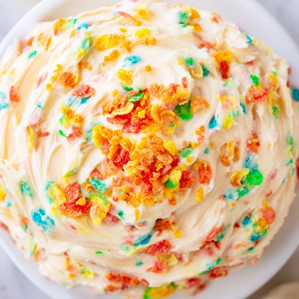 Fluffy vanilla frosting swirled with rainbow Fruity Pebbles cereal on freshly baked desserts