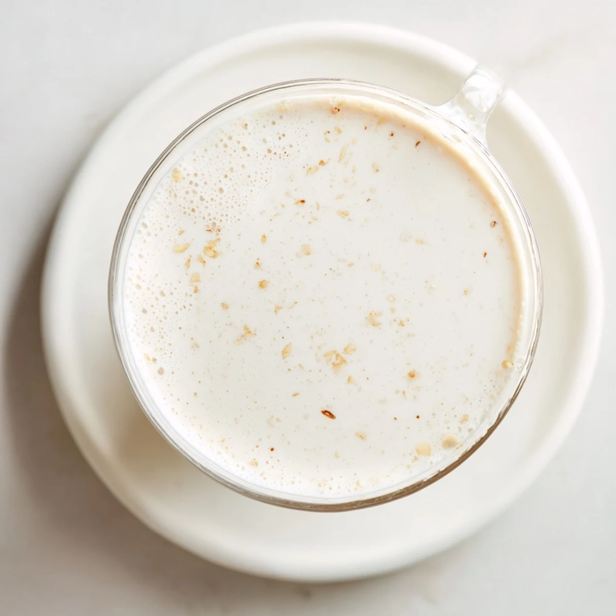 Glass of creamy homemade almond milk with vanilla bean on rustic wooden kitchen counter