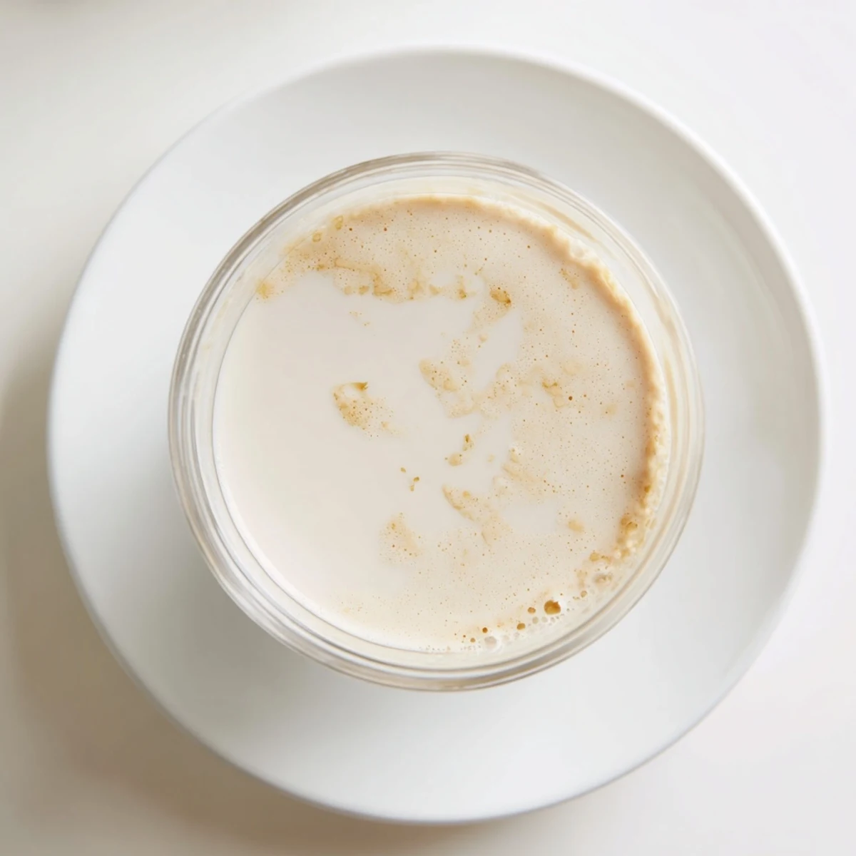 Smooth white almond milk swirling in glass jar beside raw soaked almonds and blender