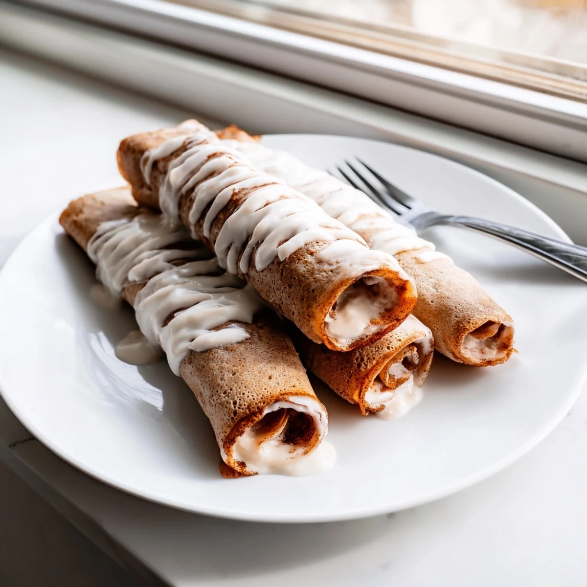 Thin cinnamon roll protein crepes rolled with creamy cinnamon filling and drizzled sweet vanilla glaze