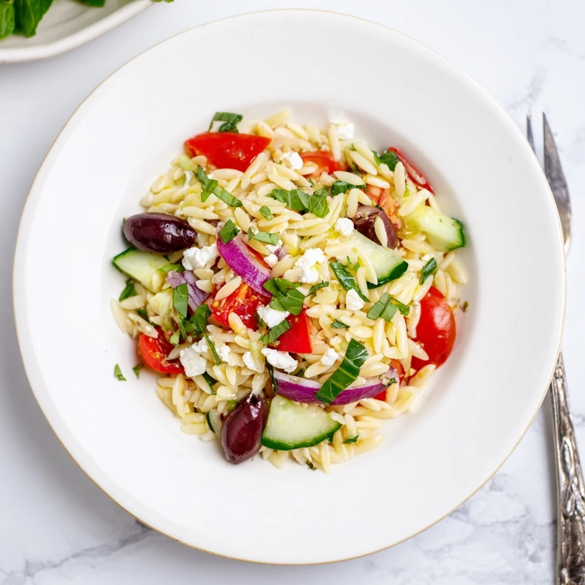 Juicy Mediterranean Orzo Pasta Salad in a bright white bowl with feta and herbs