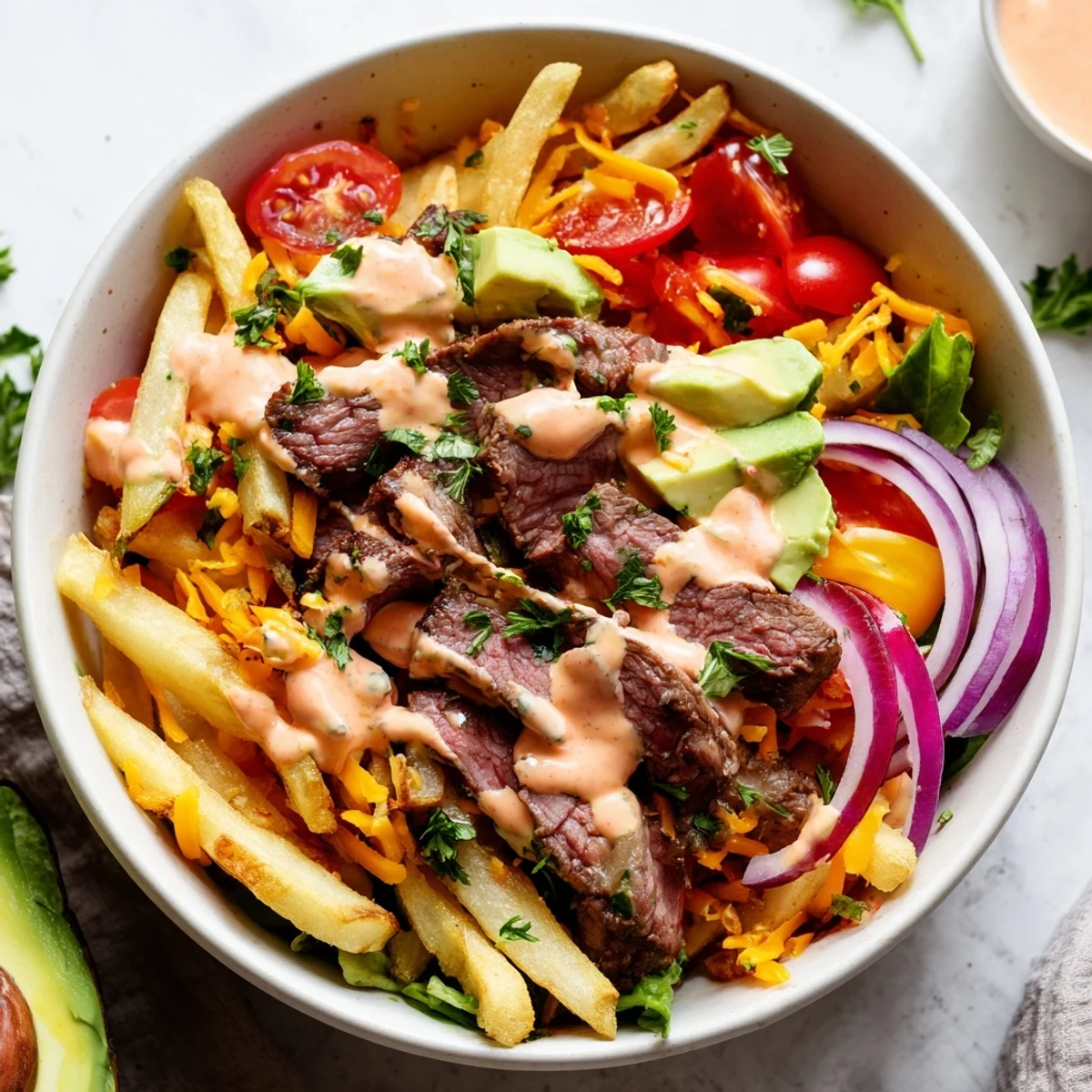 Tender seared steak strips piled over crunchy fries with fresh avocado and tomatoes