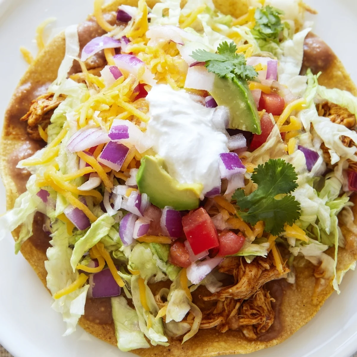 Crispy Chicken Tostadas piled with fresh lettuce, cheese, and creamy toppings.