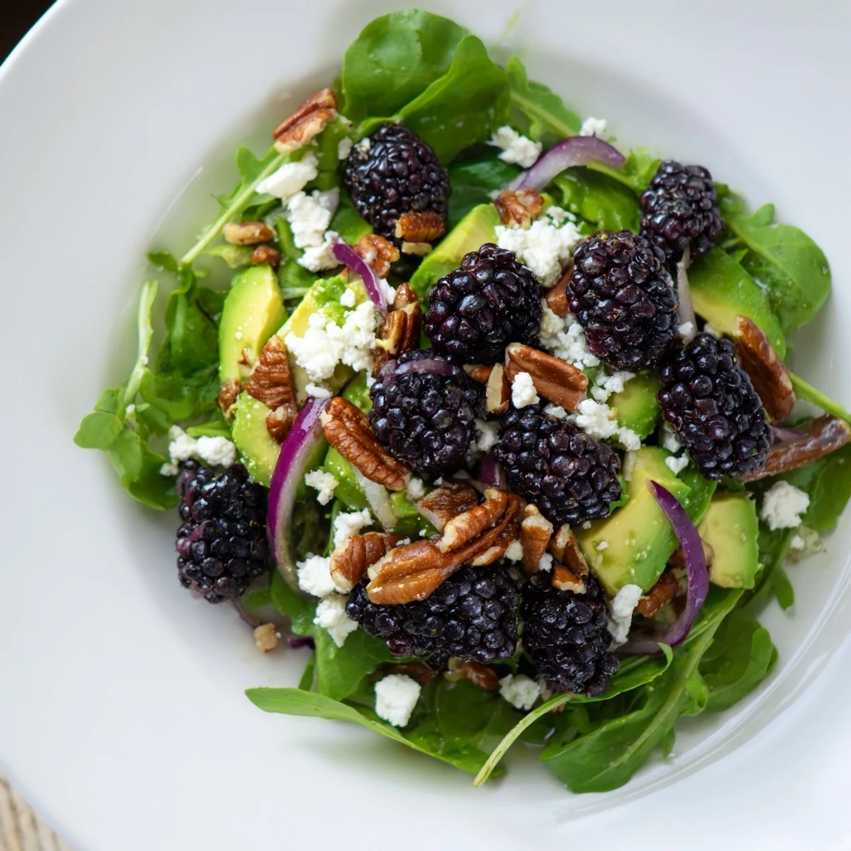 Vibrant blackberry avocado salad topped with toasted pecans and red onion slices  