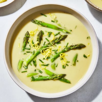 A steaming bowl of creamy asparagus soup awaits, with a swirl of fresh cream and bright lemon.